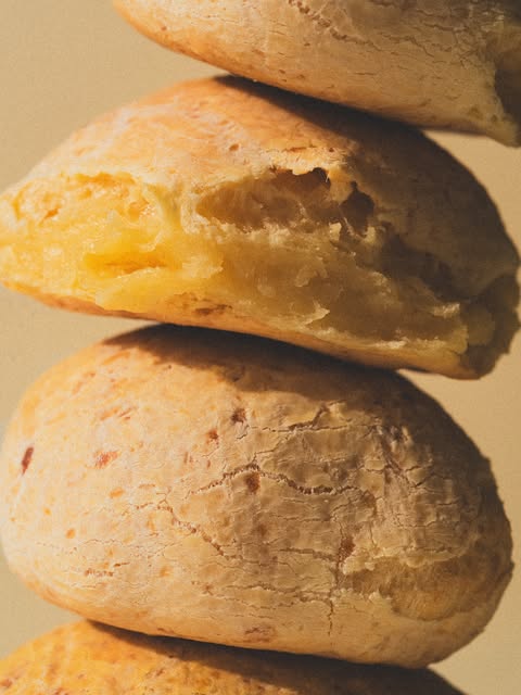 Pães de queijo empilhados, em close, dourados, com a massa macia à mostra.