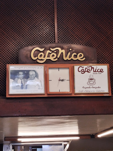 Letreiro dourado em letra cursiva escrito Café Nice, sobre painel de madeira escura.