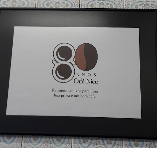 Quadro preto com o cartaz dos 80 anos do Café Nice: um 8 formado por duas xícaras e um 0 em forma de grão de café, e a frase Reunindo amigos para uma boa prosa e um bom café.